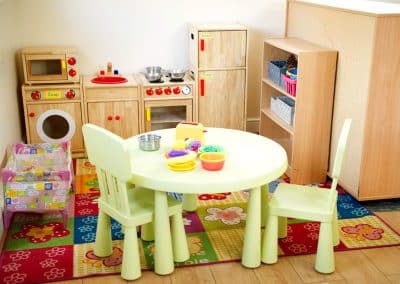 Bright cosy room in Cambridge nursery, table with kids chairs and food toys, wooden kitchen with microwave, washing machine and fridge