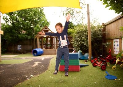 girl jumping, playing outside in the garden in Cambridge nursery. Garden space with outside toys