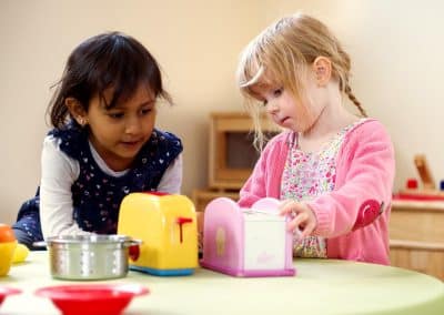 Two girls playing with kitchen toys in Cambridge nursery